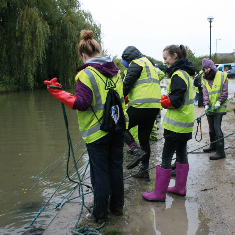 Volunteers in hi viz jackets standing next to the canal with grappling hooks