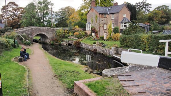 Canal with bridge, people sitting on bench and house in the background